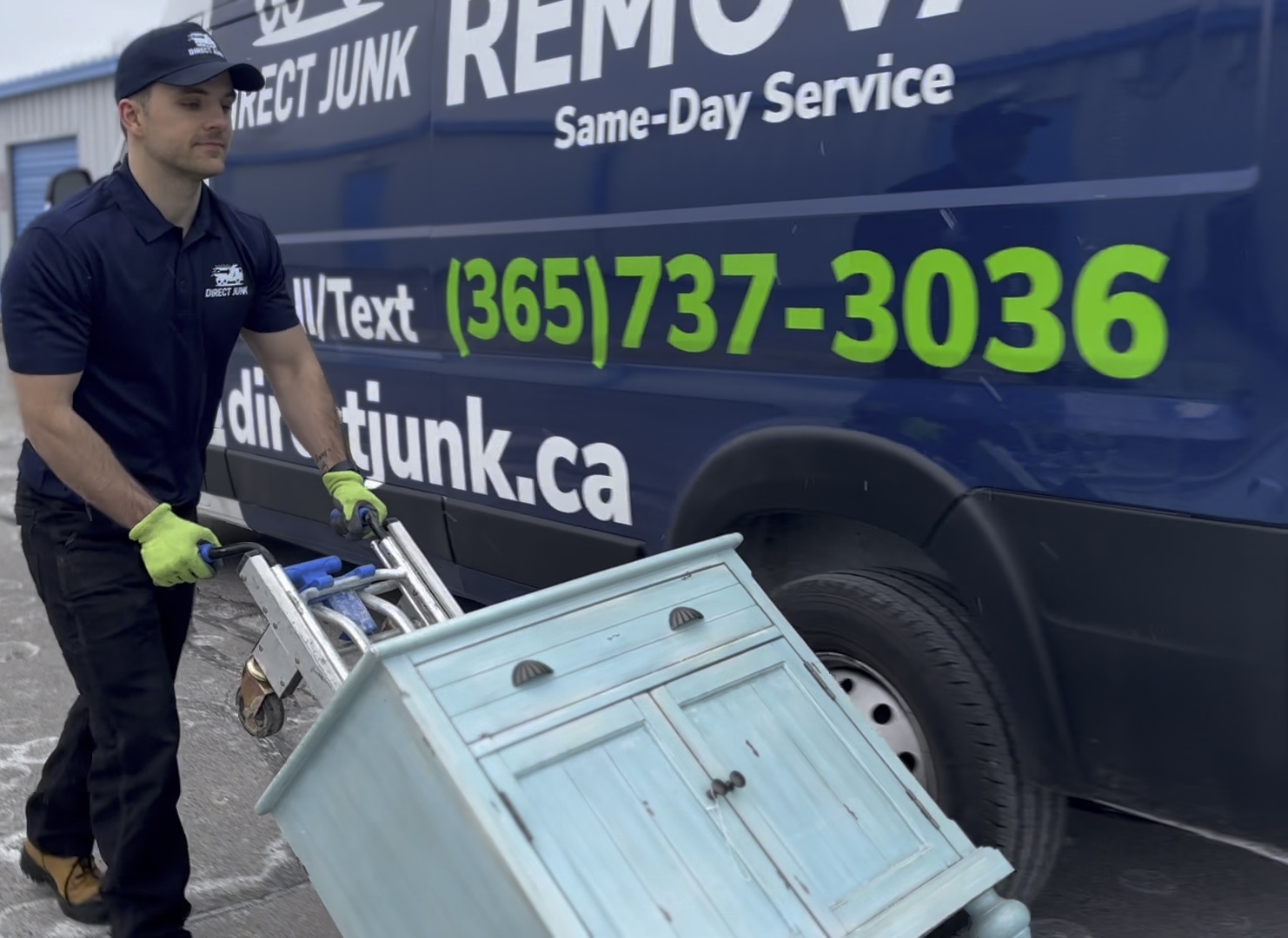 Direct Junk crew removing heavy furniture and appliances with a dolly beside branded truck
